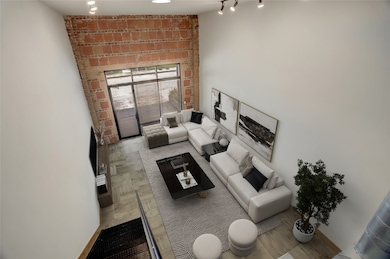 The second-floor vantage showcases the dramatic scale of the living area below. The soaring ceilings, exposed brick, and a wall of windows that floods the space with natural light. Carport can be accessed through the glass door. A true open-concept design with modern industrial character. This photo is virtually staged.