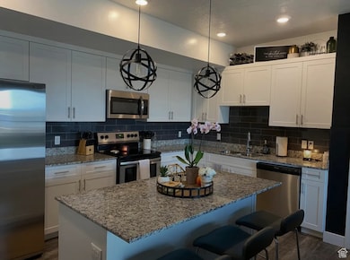Kitchen featuring stainless steel appliances, a kitchen island, a breakfast bar, white cabinetry, and backsplash