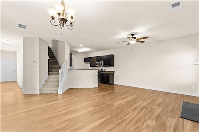 Unfurnished living room with light wood finished floors, a chandelier, stairway, and ceiling fan