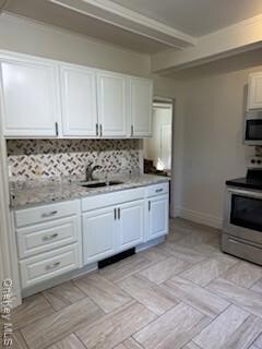 Kitchen with tasteful backsplash, stove, white cabinetry, beamed ceiling, and light stone countertops