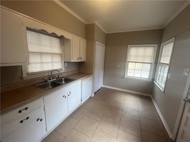 Kitchen featuring a sink, white dishwasher, white cabinetry, crown molding, and baseboards