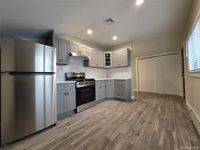 Kitchen with gray cabinets, stainless steel appliances, light countertops, decorative backsplash, and recessed lighting