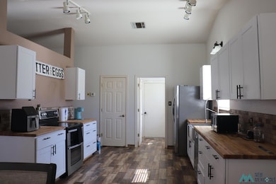 Kitchen with butcher block countertops, white cabinets, stainless steel appliances, decorative backsplash, and track lighting