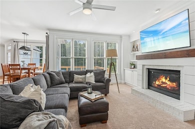 Living room with a ceiling fan, a brick fireplace, carpet flooring, built in shelves, and ornamental molding