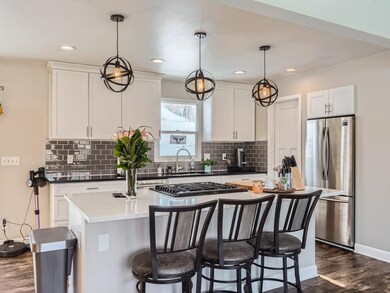 Updated kitchen with white cabinets, center island with quartz top, subway tile backsplash, stainless steel appliances, and a pantry closet.
