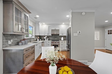 Kitchen featuring under cabinet range hood, a sink, appliances with stainless steel finishes, ornamental molding, and tasteful backsplash