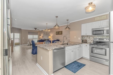Kitchen with a chandelier, appliances with stainless steel finishes, ornamental molding, white cabinetry, and a peninsula