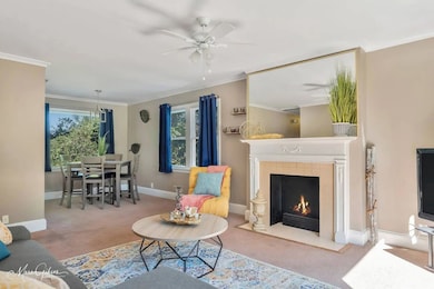 Living room featuring carpet floors, crown molding, a fireplace, and ceiling fan
