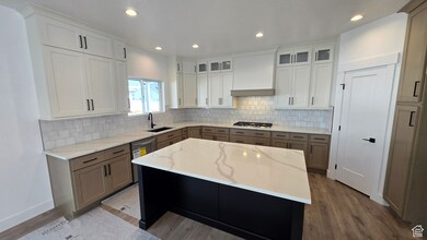 Kitchen featuring white cabinetry, light stone counters, recessed lighting, decorative backsplash, and dark wood-type flooring