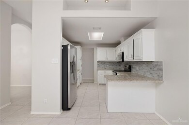 Kitchen with appliances with stainless steel finishes, white cabinets, a peninsula, decorative backsplash, and light tile patterned floors