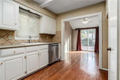 View from the kitchen into the dining area, featuring wood flooring, stainless steel dishwasher, and access to the back deck through sliding doors.