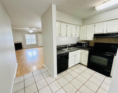 Kitchen featuring dark countertops, white cabinets, black appliances, a textured ceiling, and light tile patterned floors