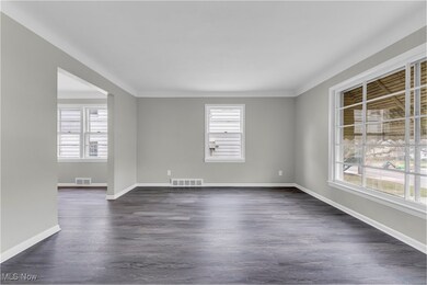 Empty room with a wealth of natural light, visible vents, and dark wood-style floors