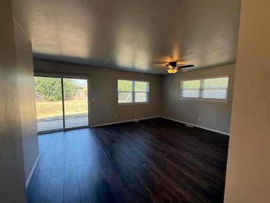 Empty room with a textured ceiling, dark wood-style flooring, and a ceiling fan