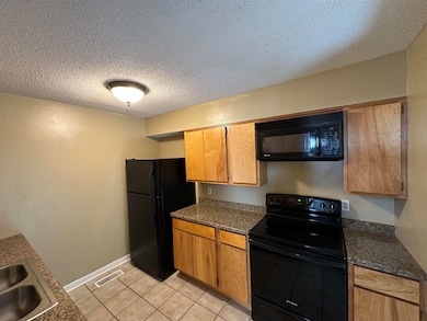 Kitchen featuring black appliances, dark countertops, light tile patterned flooring, and a textured ceiling