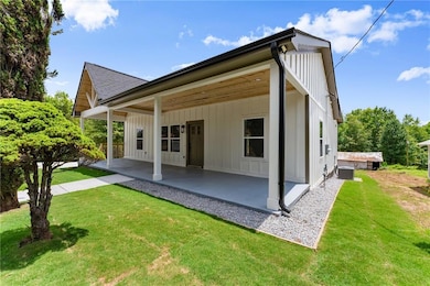 Back of house with a patio area, a lawn, roof with shingles, and board and batten siding