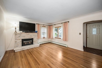 Unfurnished living room featuring wood finished floors, arched walkways, a fireplace, and a baseboard heating unit