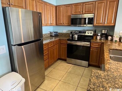 Kitchen with dark stone countertops, stainless steel appliances, brown cabinets, and light tile patterned floors
