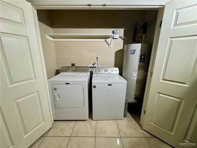 Clothes washing area featuring light tile patterned floors, laundry area, water heater, and separate washer and dryer