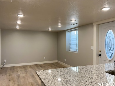 Foyer with baseboards, visible vents, light wood-style floors, and a textured ceiling