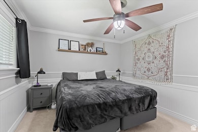 Bedroom with crown molding, light colored carpet, wainscoting, and ceiling fan