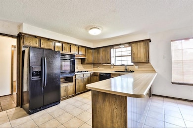 Kitchen featuring black appliances, a peninsula, a sink, a textured ceiling, and light countertops