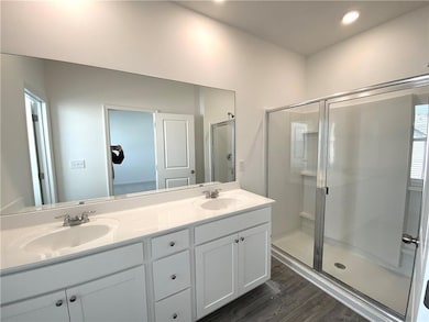 Bathroom with double vanity, wood finished floors, a stall shower, and recessed lighting