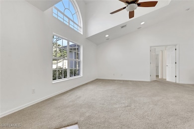 Unfurnished living room with light carpet, a high ceiling, and ceiling fan