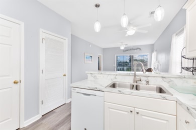 Kitchen with dishwasher, a sink, light countertops, light wood-type flooring, and white cabinetry