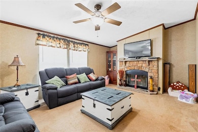 Living area with light colored carpet, crown molding, a ceiling fan, a stone fireplace, and lofted ceiling