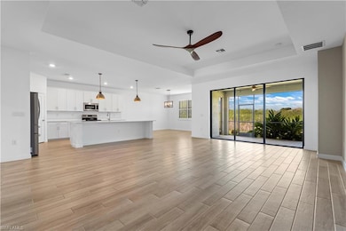 Unfurnished living room featuring a tray ceiling, ceiling fan, light wood-style flooring, and recessed lighting