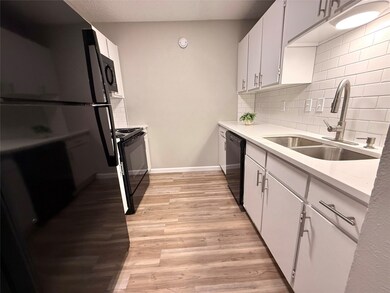 Kitchen with white cabinetry, black appliances, light wood-style floors, decorative backsplash, and light stone counters