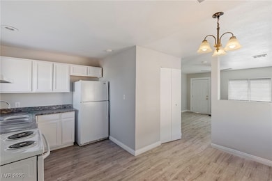 Kitchen with white cabinetry, white appliances, light wood-type flooring, and hanging light fixtures