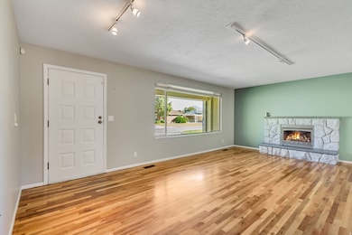 Unfurnished living room with rail lighting, a stone fireplace, light wood finished floors, and a textured ceiling