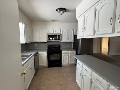 Kitchen featuring appliances with stainless steel finishes, white cabinetry, light tile patterned floors, and light countertops