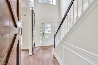 Foyer with a barn door, light wood-style floors, a decorative wall, a high ceiling, and a wainscoted wall