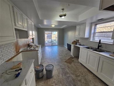 Kitchen featuring backsplash, a tray ceiling, white cabinetry, dark wood-style flooring, and light stone countertops