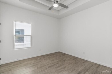 Unfurnished room featuring light wood-style floors, baseboards, ceiling fan, and a tray ceiling