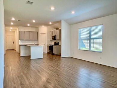 Kitchen featuring dark wood-style flooring, appliances with stainless steel finishes, tasteful backsplash, a center island with sink, and gray cabinetry