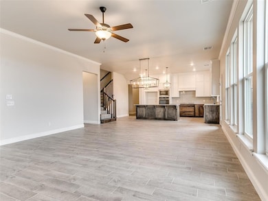 Unfurnished living room with ornamental molding, wood tiled floors, ceiling fan, stairs, and a chandelier