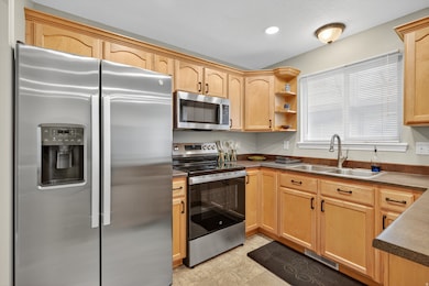 Kitchen with appliances with stainless steel finishes, light brown cabinetry, open shelves, and dark countertops