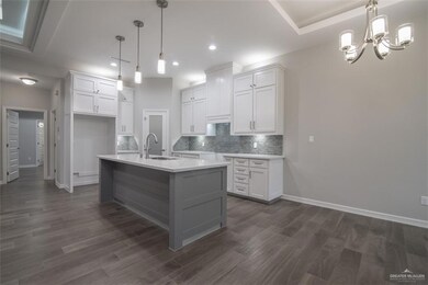 Kitchen featuring dark hardwood / wood-style floors, pendant lighting, sink, white cabinets, and a kitchen island with sink