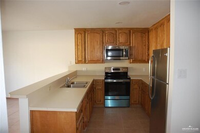 Kitchen featuring brown cabinetry, stainless steel appliances, light tile patterned flooring, light countertops, and a peninsula