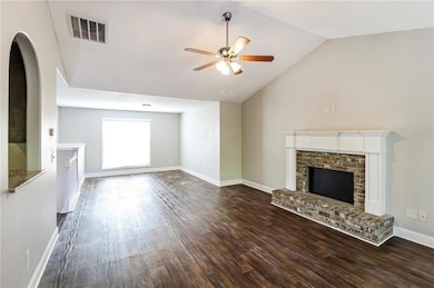 Unfurnished living room with ceiling fan, a brick fireplace, dark wood-type flooring, vaulted ceiling, and arched walkways