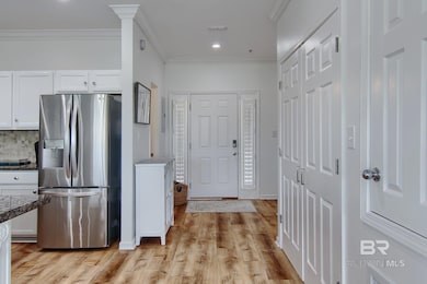 Kitchen with stainless steel refrigerator with ice dispenser, white cabinets, ornamental molding, light wood-style floors, and backsplash