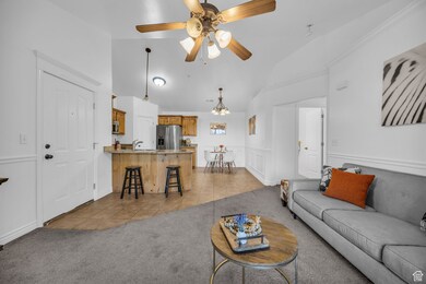 Living room featuring light tile patterned flooring, light carpet, a ceiling fan, high vaulted ceiling, and a chandelier