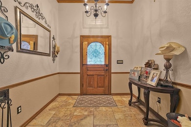 Entrance foyer featuring stone tile floors, crown molding, a chandelier, baseboards, and a textured wall