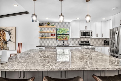 Kitchen with tasteful backsplash, a breakfast bar area, light stone countertops, white cabinetry, and appliances with stainless steel finishes