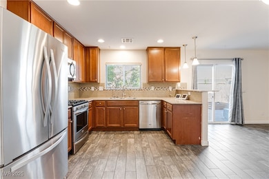 Kitchen with appliances with stainless steel finishes, brown cabinetry, backsplash, a peninsula, and recessed lighting