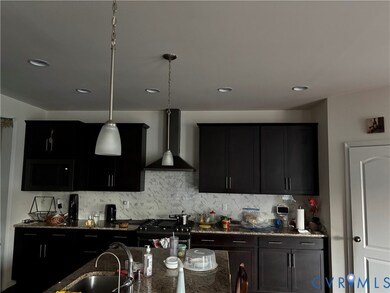 Kitchen with dark cabinets, dark stone counters, wall chimney range hood, pendant lighting, and range with gas stovetop